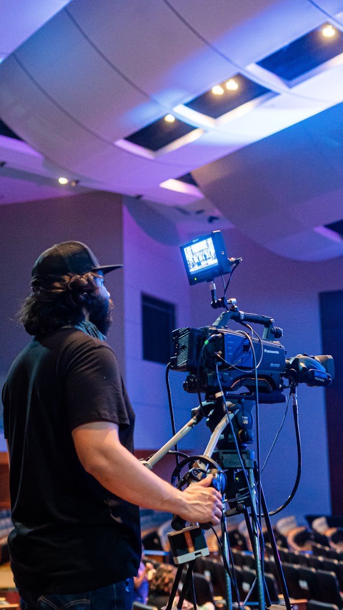 Back view of bearded camera man recording stage during music performance in illuminated concert hall
